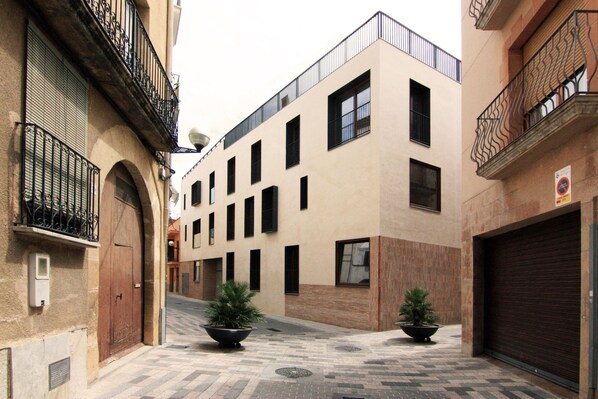 A narrow street with a building featuring a modern facade, large windows, and a gated entrance.