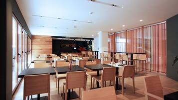 A modern restaurant with a long counter, wooden chairs, and tables.