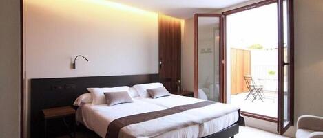 Un dormitorio moderno con una cama grande, mesitas de noche y un ventanal corredero que da a un balcón.