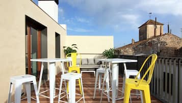 An outdoor patio with white and yellow chairs and tables, a stone wall, and a view of a historic building in the background.