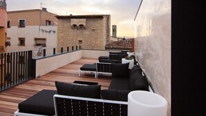 A rooftop terrace with a long black sofa, white cushions, and a white table. - Hotel Raval de la Mar (Vila-Seca)