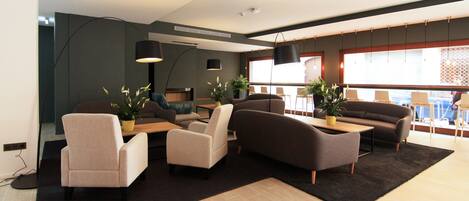 Una sala de estar moderna con sofás, sillones y una mesa de centro. Hay plantas en macetas y lámparas colgantes.
