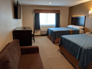 Een hotelkamer met twee bedden, een bureau, een stoel en een aan de muur bevestigde televisie.