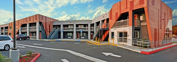 A modern building with multiple entrances, a parking lot, and a clear sky.