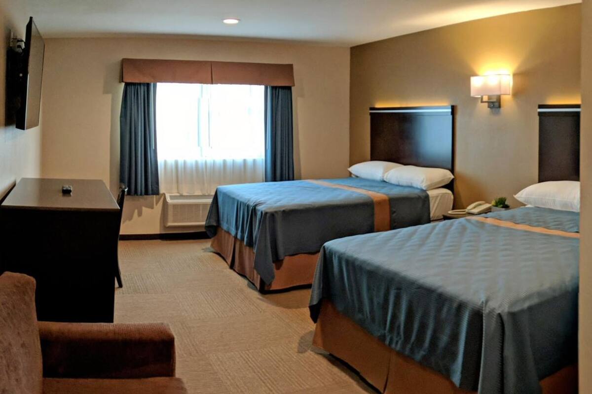 Une chambre d’hôtel avec deux lits, un bureau, une chaise et un téléviseur.