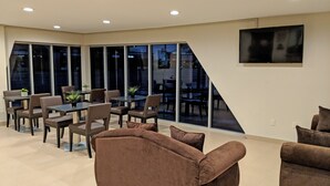 A spacious room with a dining area, large windows, and a flat-screen TV mounted on the wall. - Epic Hotel (Pico Rivera)