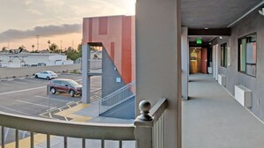 A hotel corridor with a parking lot view, a staircase, and red doors. - Epic Hotel (Pico Rivera)