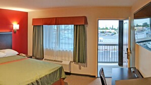 A hotel room with a bed, a desk, a chair, a window with curtains, and a view of the outside. - Epic Hotel (Pico Rivera)