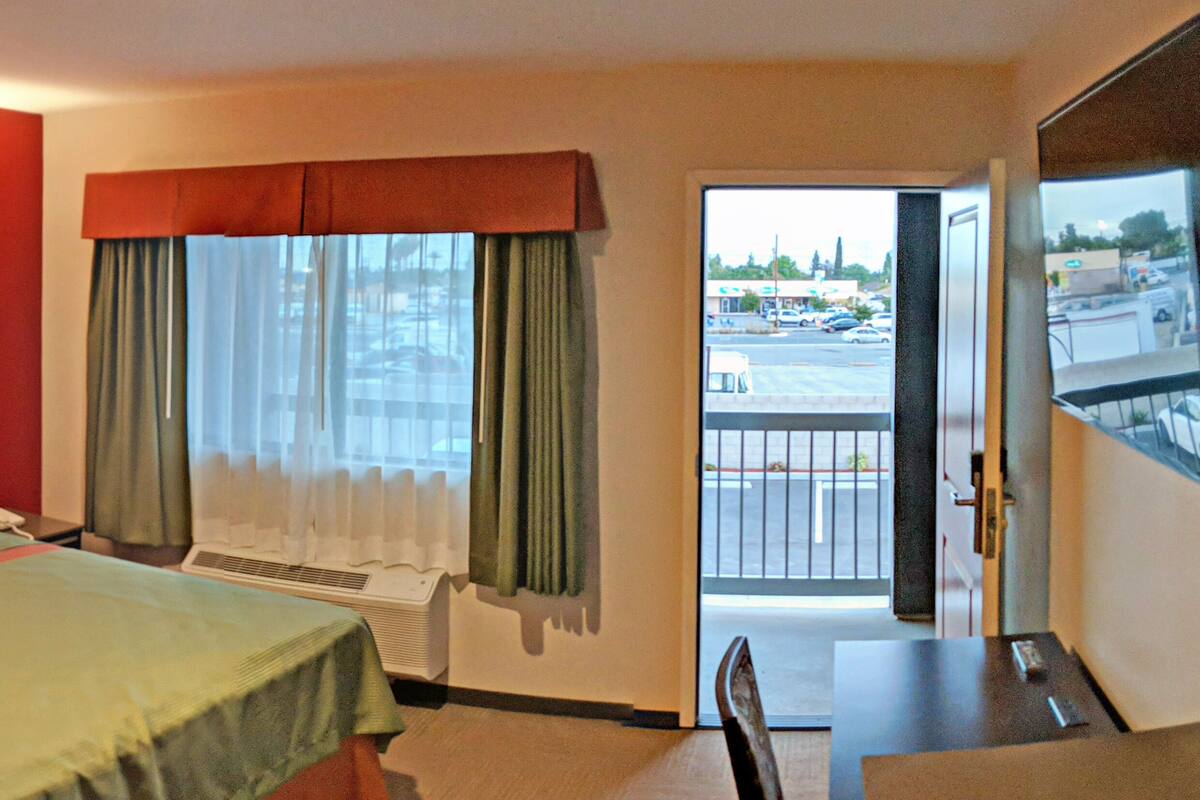 Une chambre d’hôtel avec un lit, un bureau, une chaise, une fenêtre avec des rideaux et une vue sur l’extérieur.