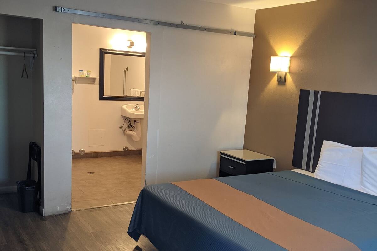 Une chambre d’hôtel avec un lit, une table de chevet et une salle de bain visible à travers une porte ouverte.