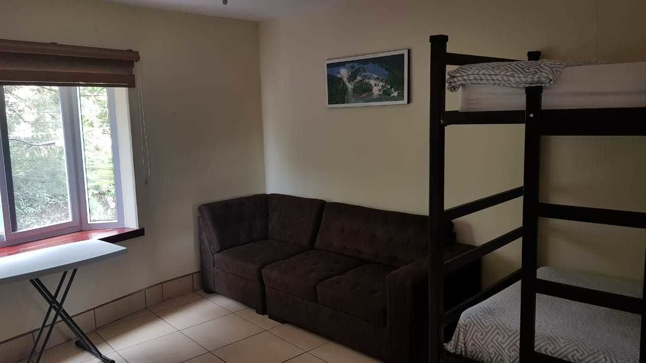 A room with a bunk bed, a sofa, a window with blinds, and a painting on the wall.
