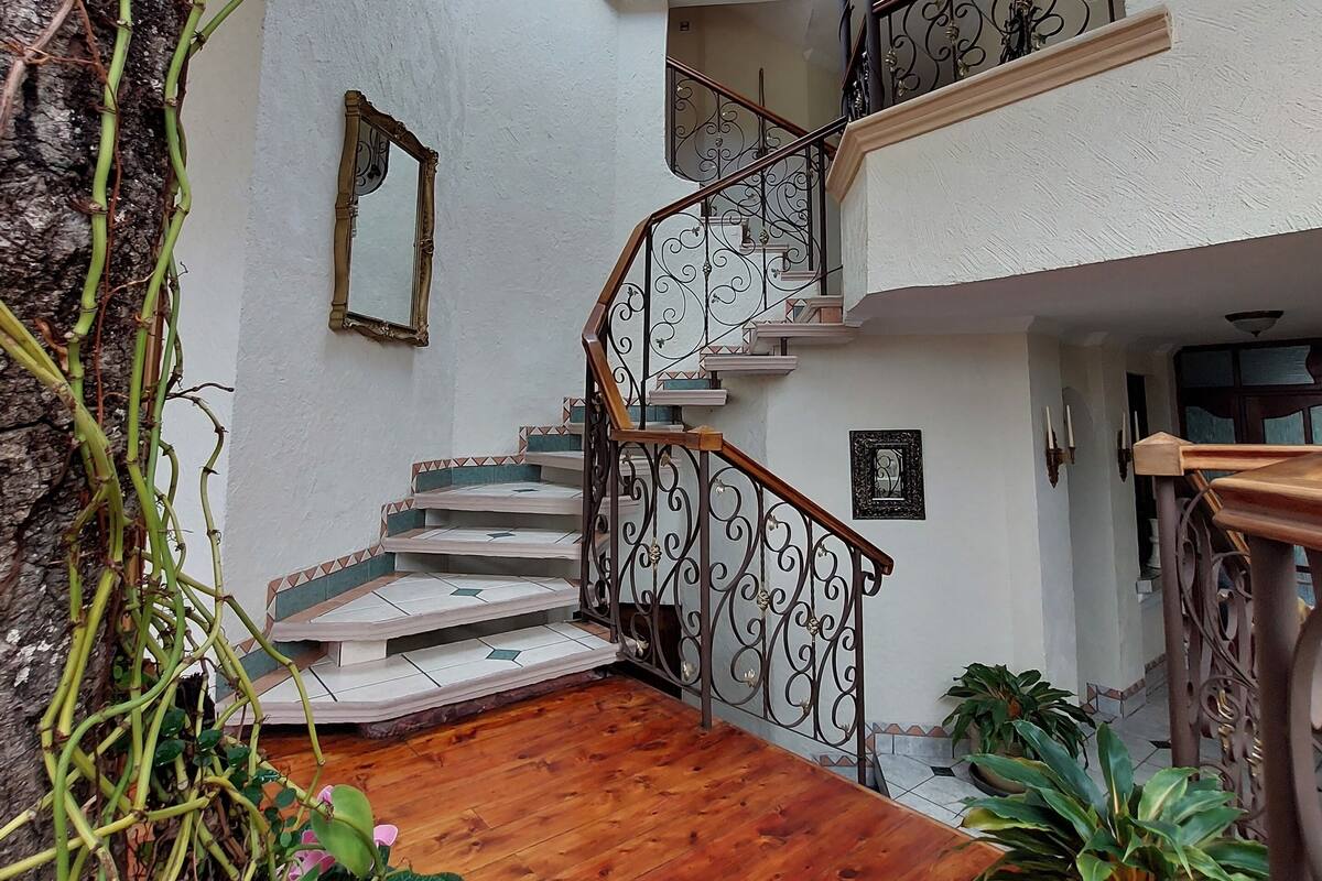 A multi-level interior with a wooden staircase, a stained glass window, and potted plants.