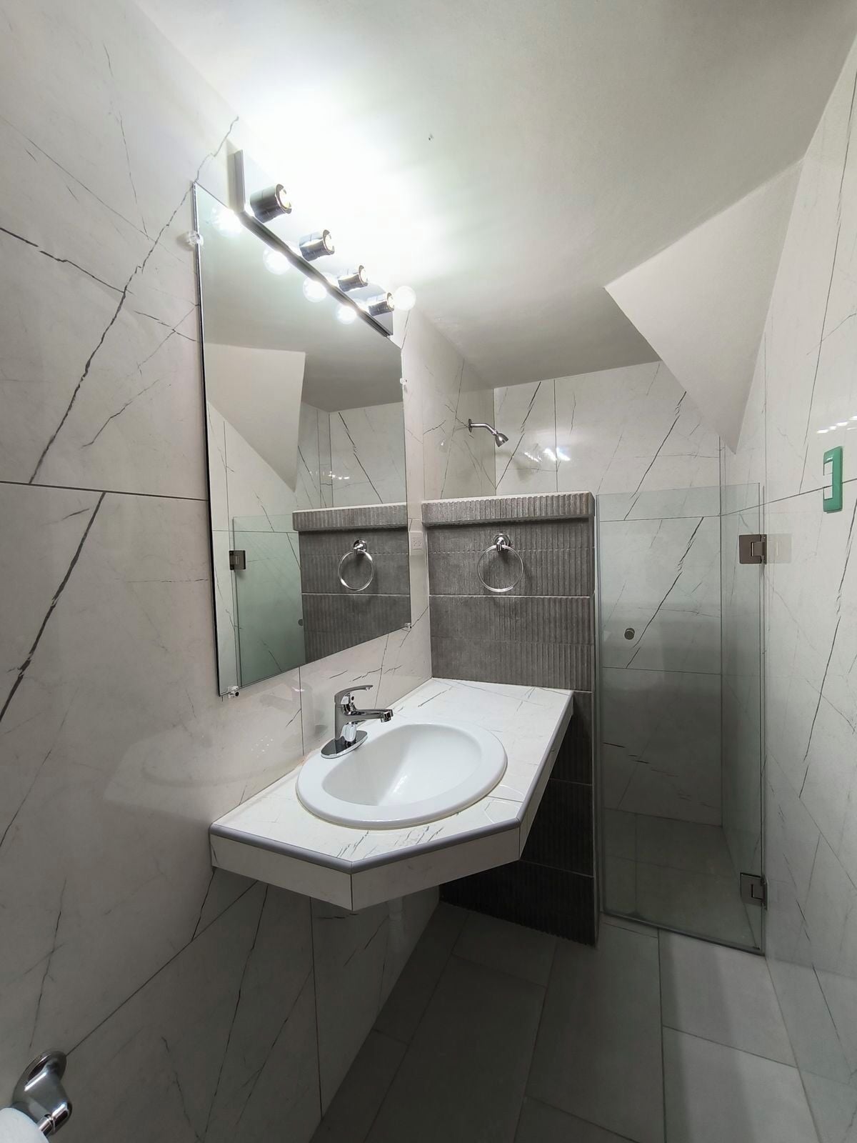 Un baño moderno con lavamanos blanco, un espejo y zona de ducha.