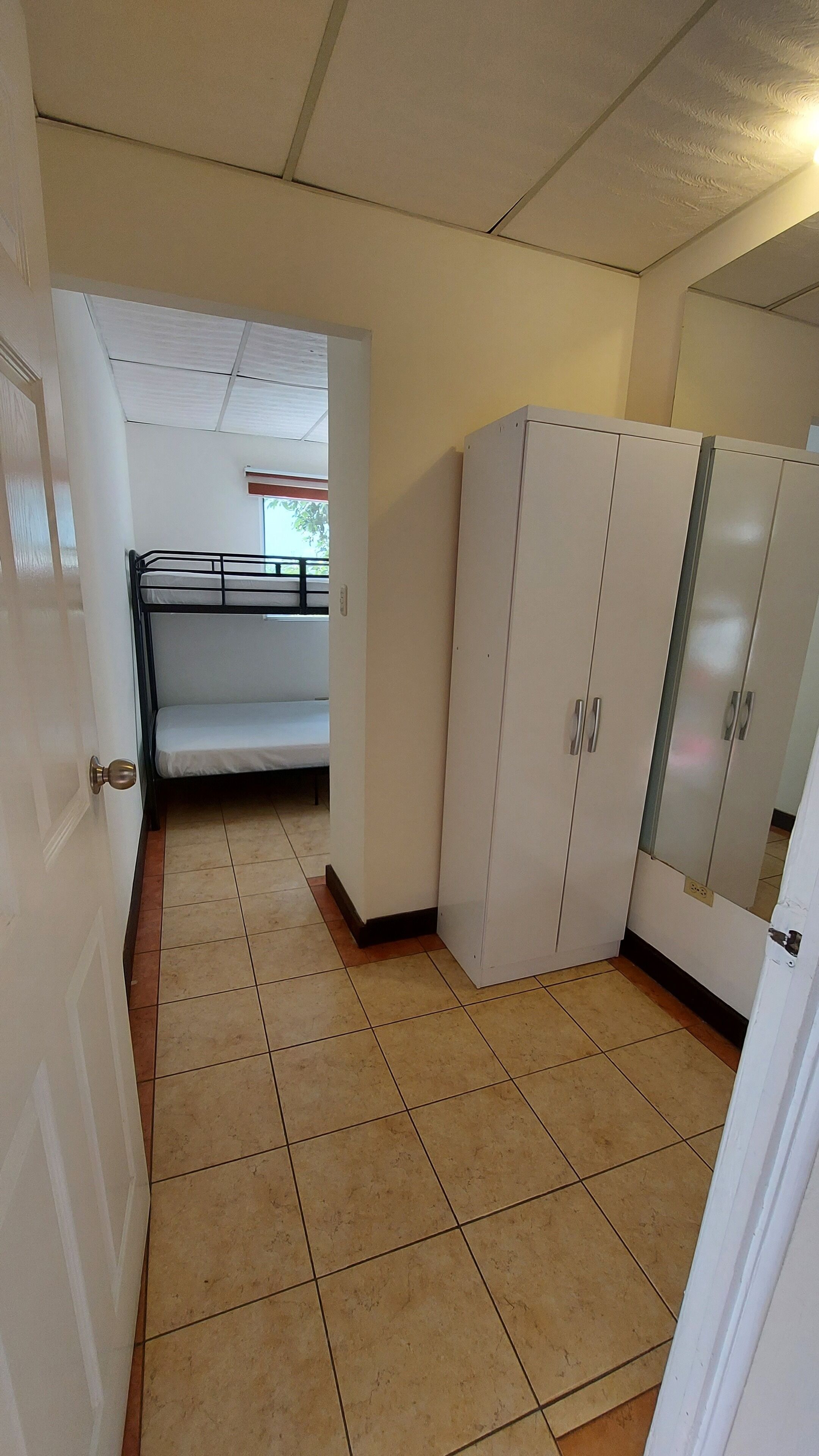 A room with a bunk bed, white wardrobe, and tiled floor.