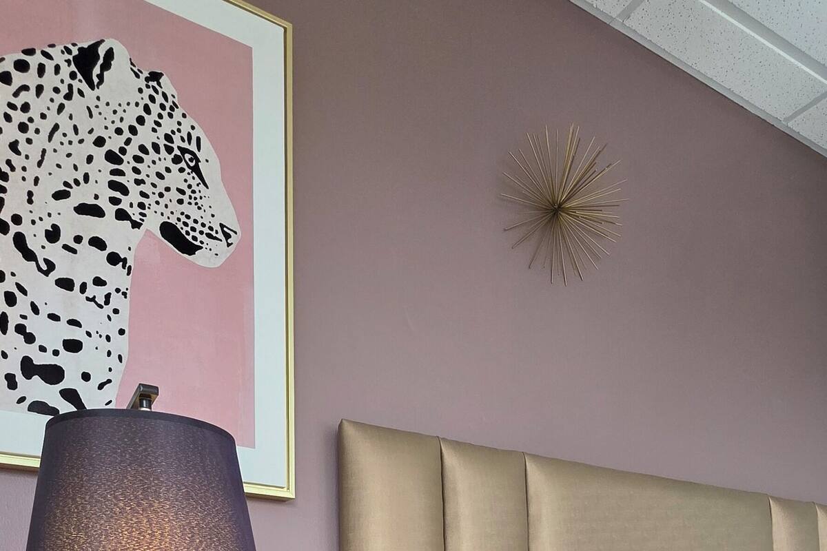 A neatly made bed with a quilted cover, a bedside lamp on a wooden nightstand, and a framed artwork of a leopard on the wall.