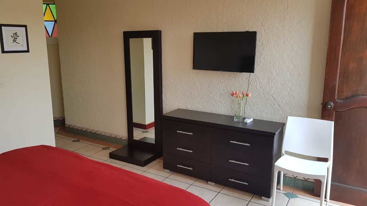 Une chambre avec un lit, une commode, un miroir, une télévision et une chaise.