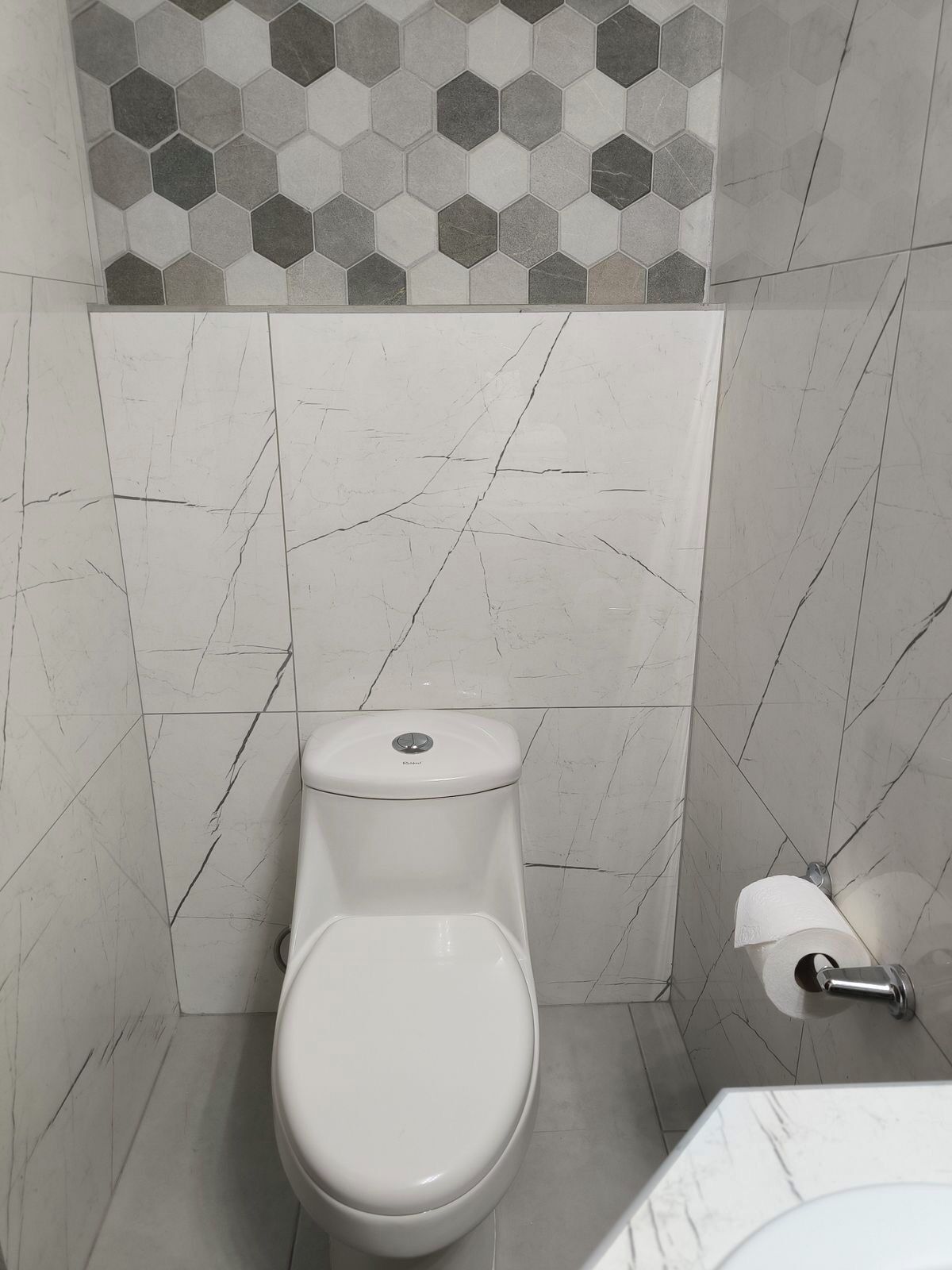 A bathroom with a toilet, a toilet paper holder, and a sink.