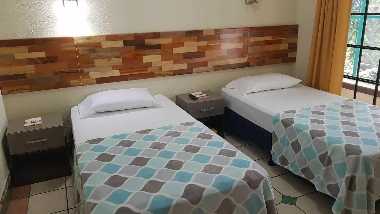 A hotel room with two beds, a wooden headboard, a nightstand, and a window with curtains.