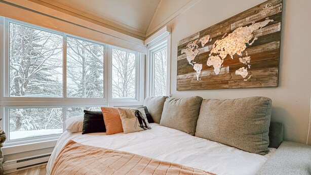 A bedroom with a large window, a bed with multiple pillows, and a world map artwork on the wall. - Le Villageois by Gestion ELITE  (Mont-Tremblant)
