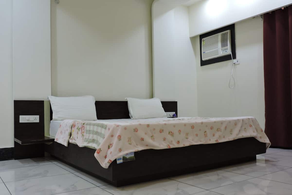 Una cama individual con una colcha estampada, una mesita de noche y un aire acondicionado instalado en la pared.