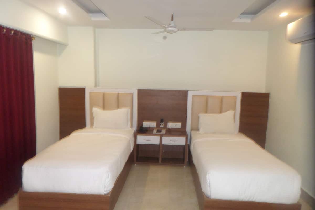 Habitación de hotel con dos camas individuales, cabecera de madera, mesita de noche con teléfono y lámpara, y ventilador de techo.