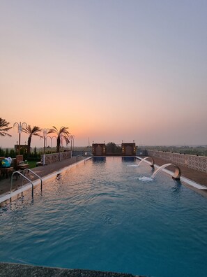 A swimming pool with a sunset view, surrounded by palm trees and lounge chairs.