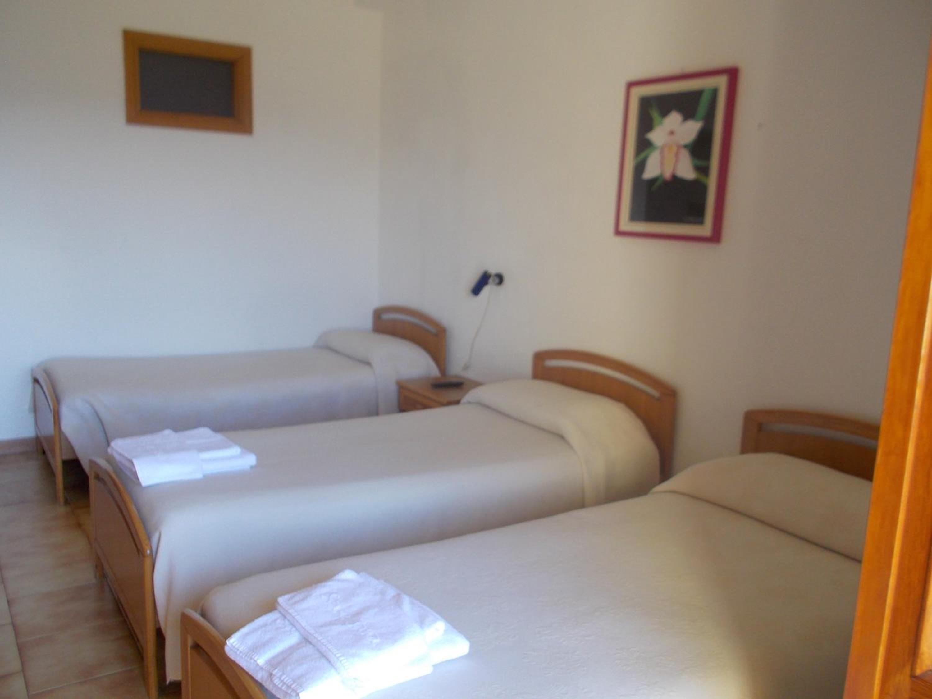 Una stanza con due letti singoli, ognuno dotato di una testiera in legno e un comodino. Sopra i letti, un quadro incorniciato appeso al muro.