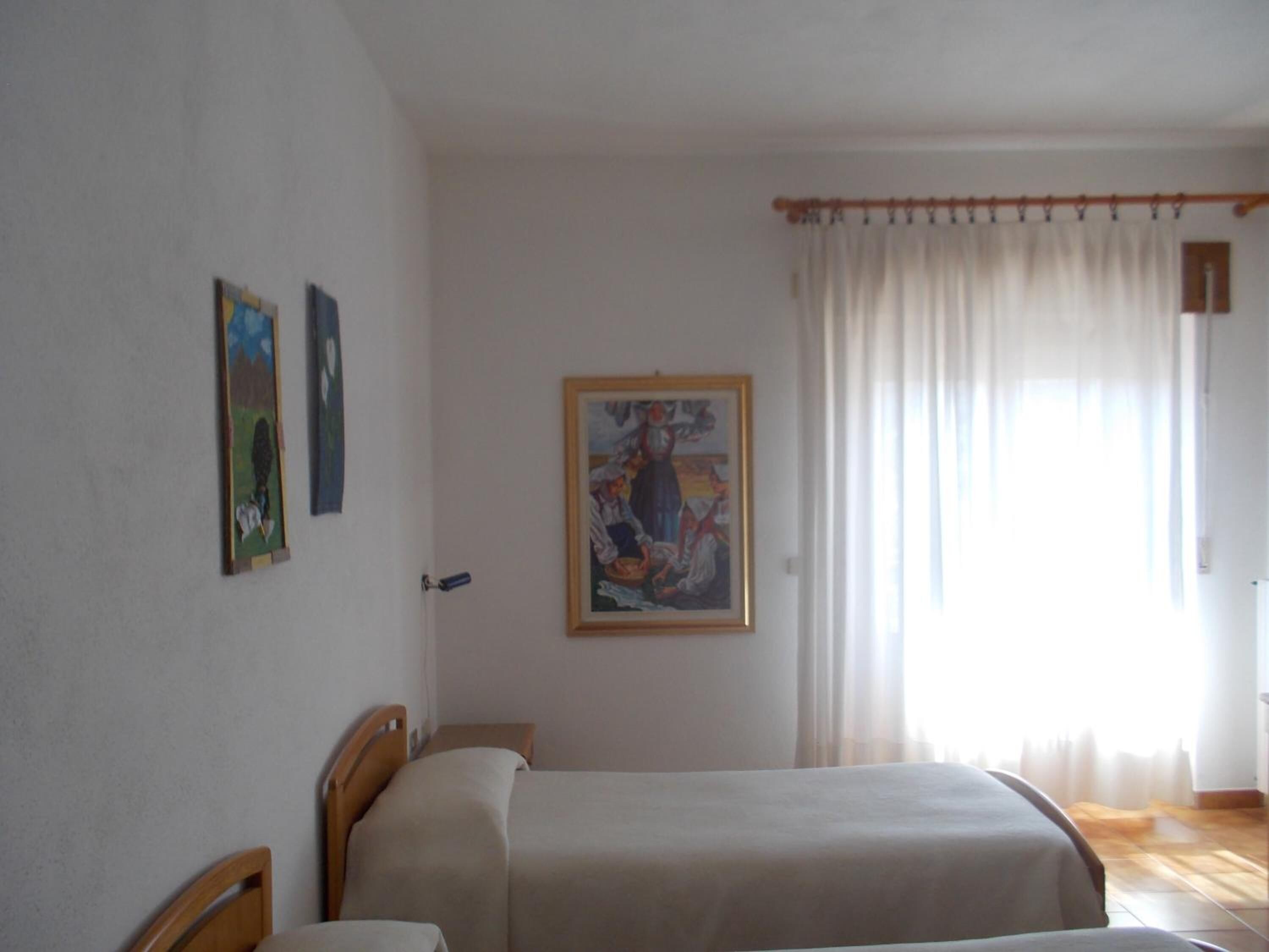 A bedroom with two beds, a painting on the wall, and a window with curtains.