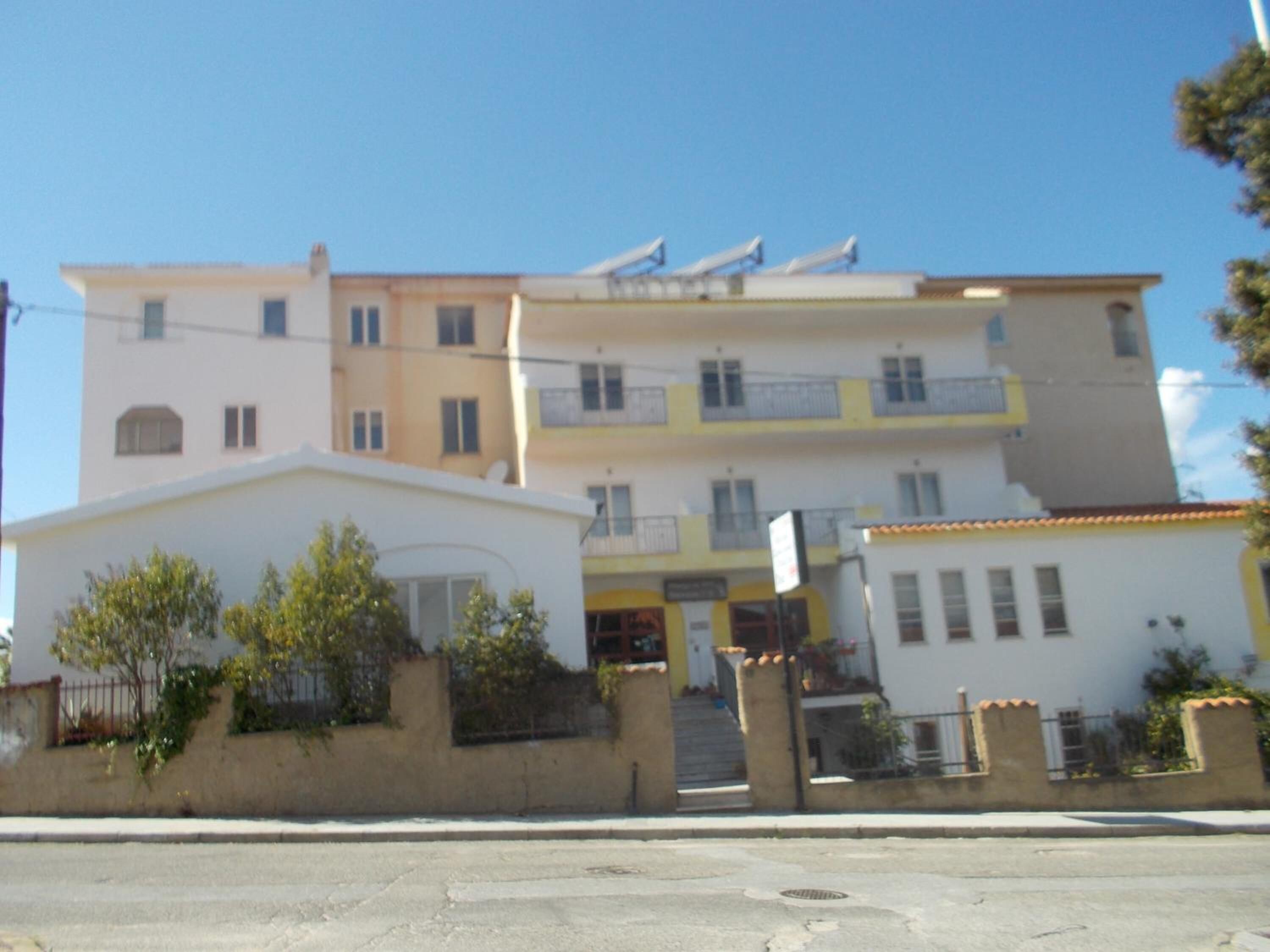 A multi-story residential building with balconies, a gated entrance, and a small front garden.