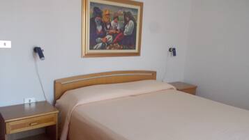 A bedroom with a wooden bed, a nightstand, a bedside table, a wall-mounted phone, and a framed painting.