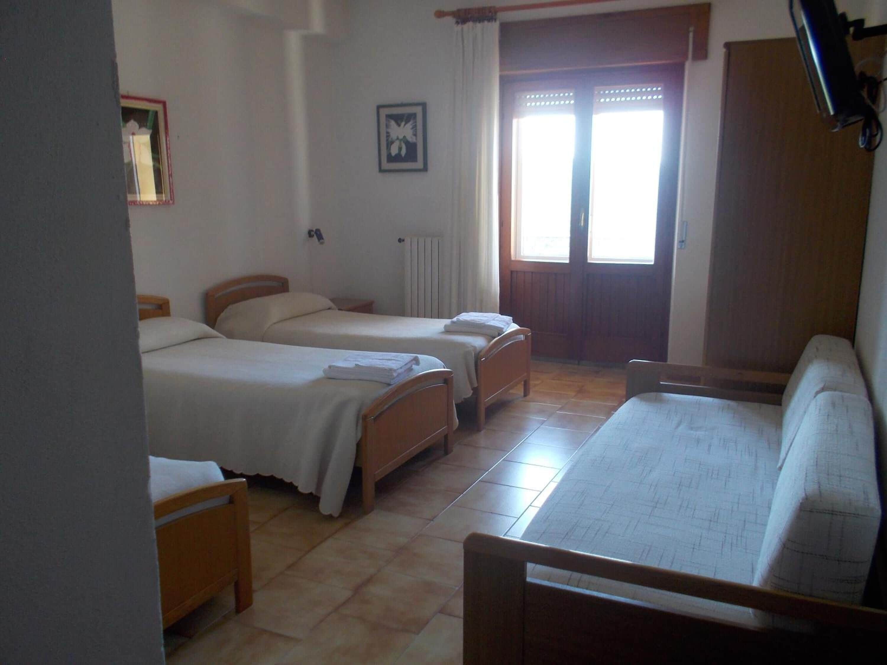 Una habitación con dos camas individuales, un sofá de madera, un radiador y una ventana con cortinas.