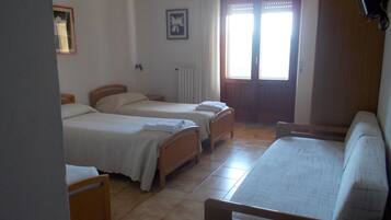Una habitación con dos camas individuales, un sofá de madera, un radiador y una ventana con cortinas.