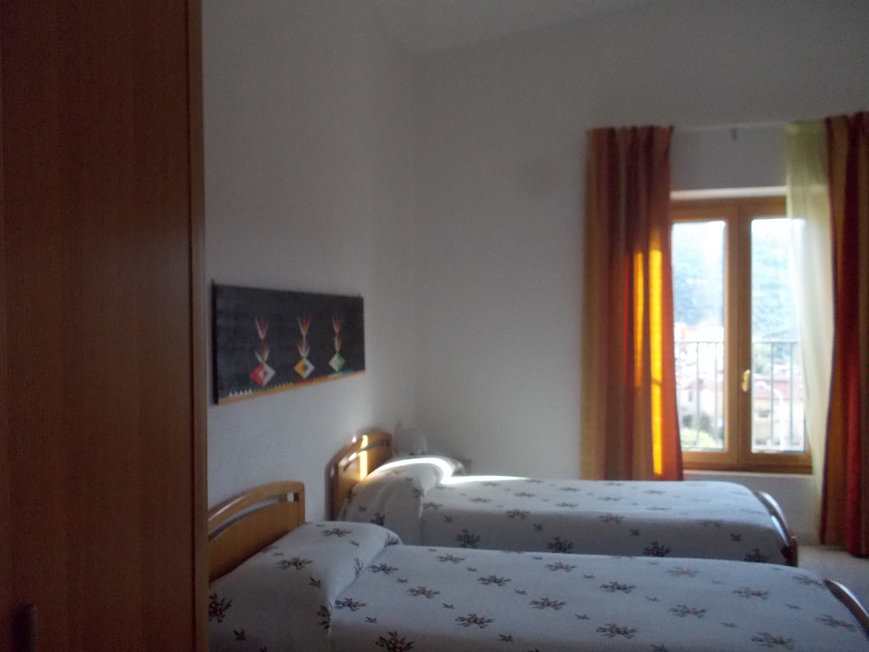 A room with two beds, a painting on the wall, and a window with curtains.