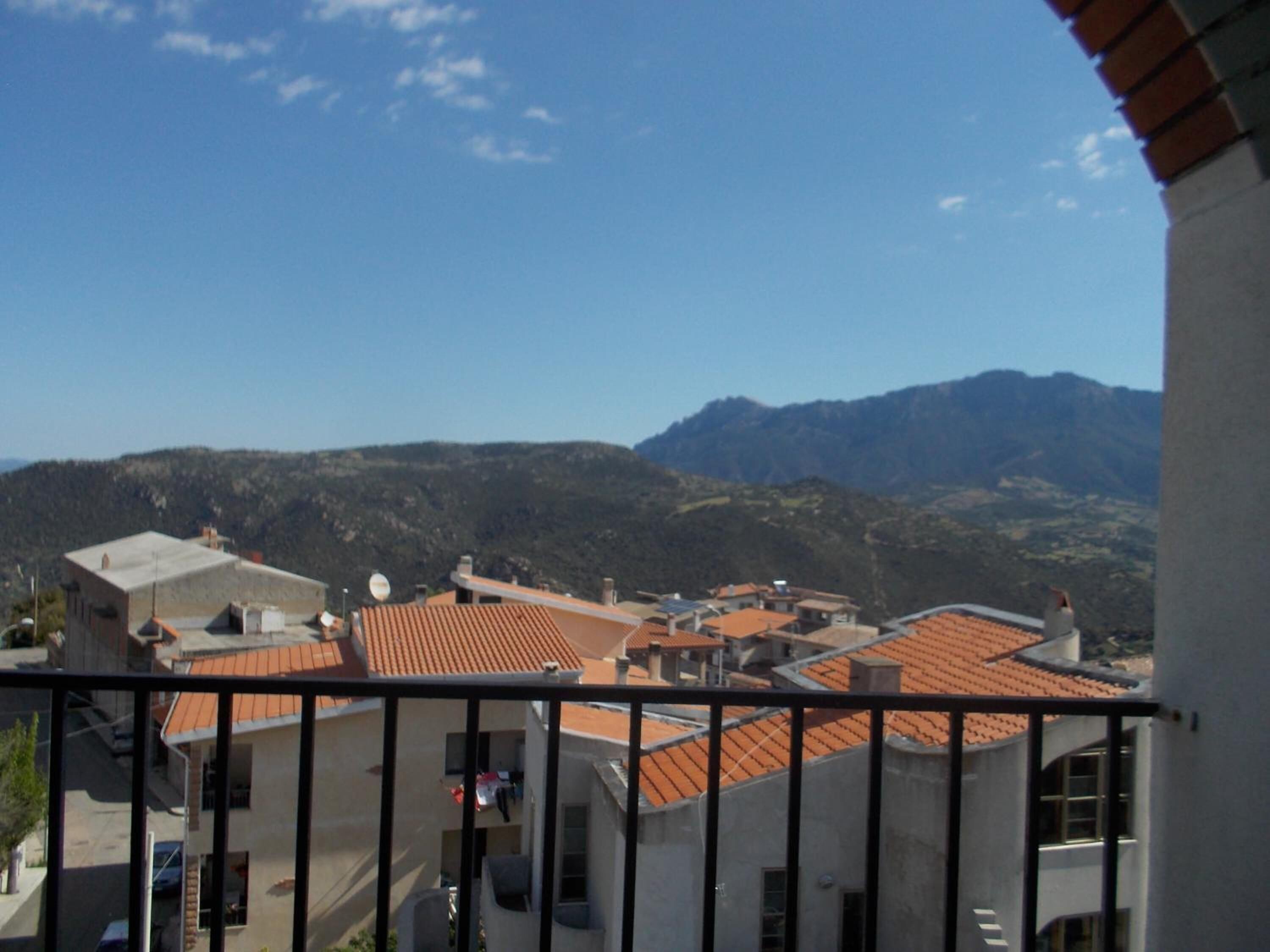 Zona residencial com edifícios de telhados em terracota, céu claro e montanhas ao fundo.