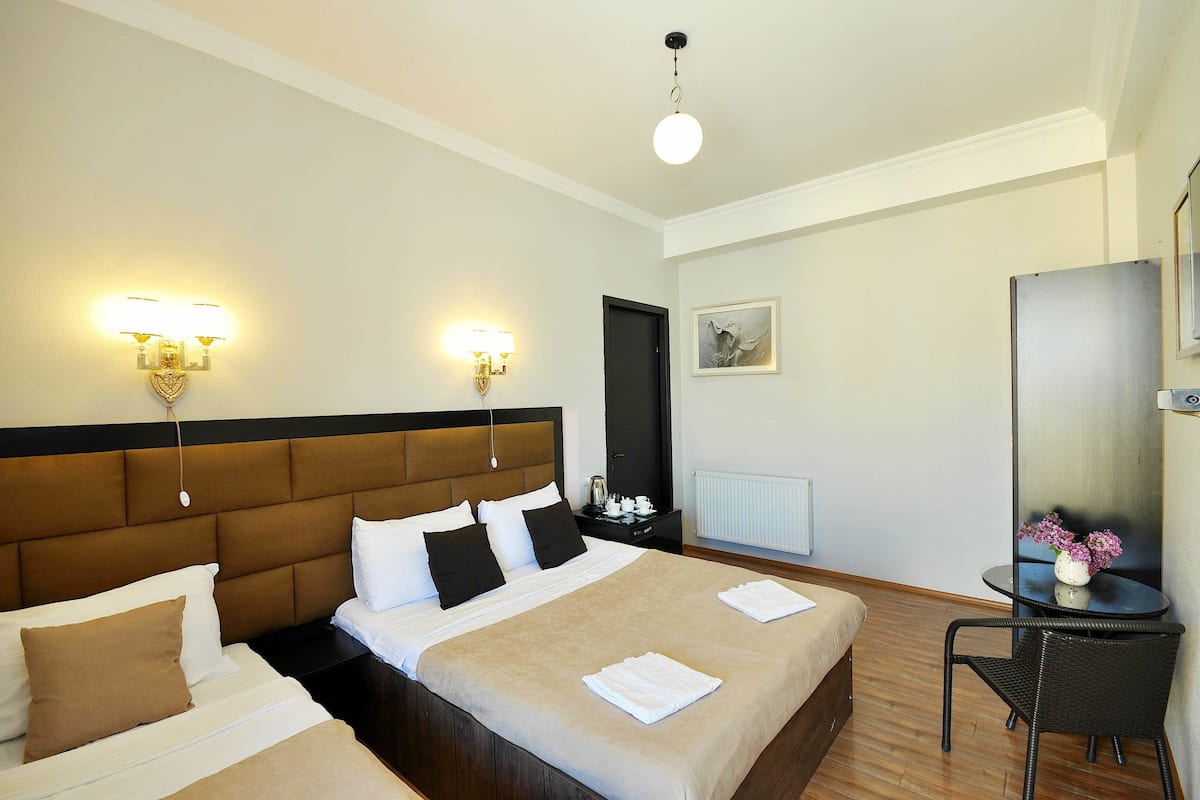 A hotel room with two beds, a nightstand, a table with a vase of flowers, and a mirror.