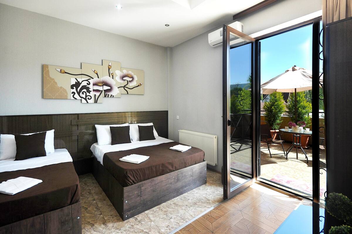 A hotel room with two beds, a large window, and a view of the outdoors.