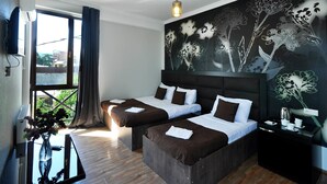 A hotel room with two beds, a large window with curtains, a wall mural, and a small table with a kettle. - Marsel Hotel (Tbilisi)