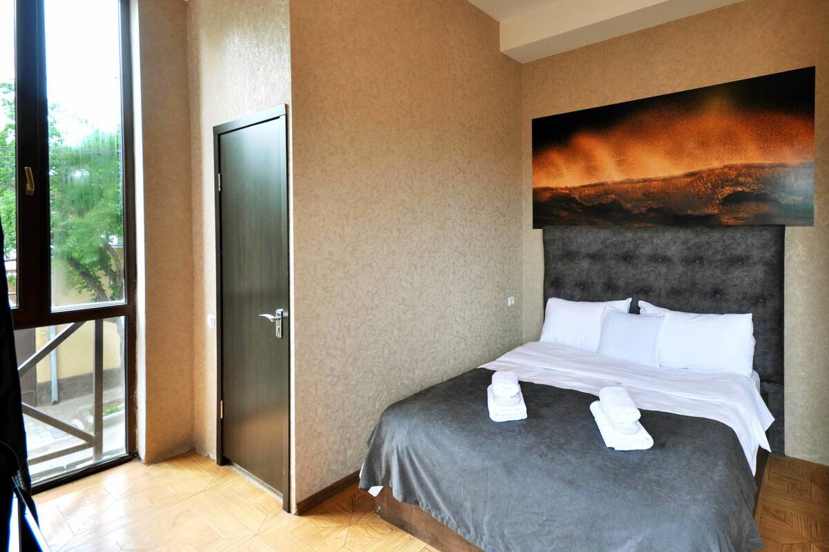 A hotel room with a large bed, a door to the outside, and a view of the outdoors.