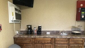 Una cocina con cafetera, dispensador de agua, cubo de basura y microondas.