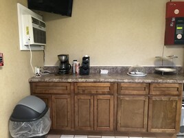 Una cocina con cafetera, dispensador de agua, cubo de basura y microondas.