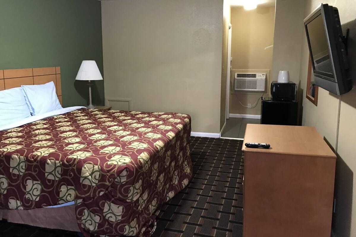 A hotel room with a bed, a desk, a lamp, a television, and an air conditioning unit.