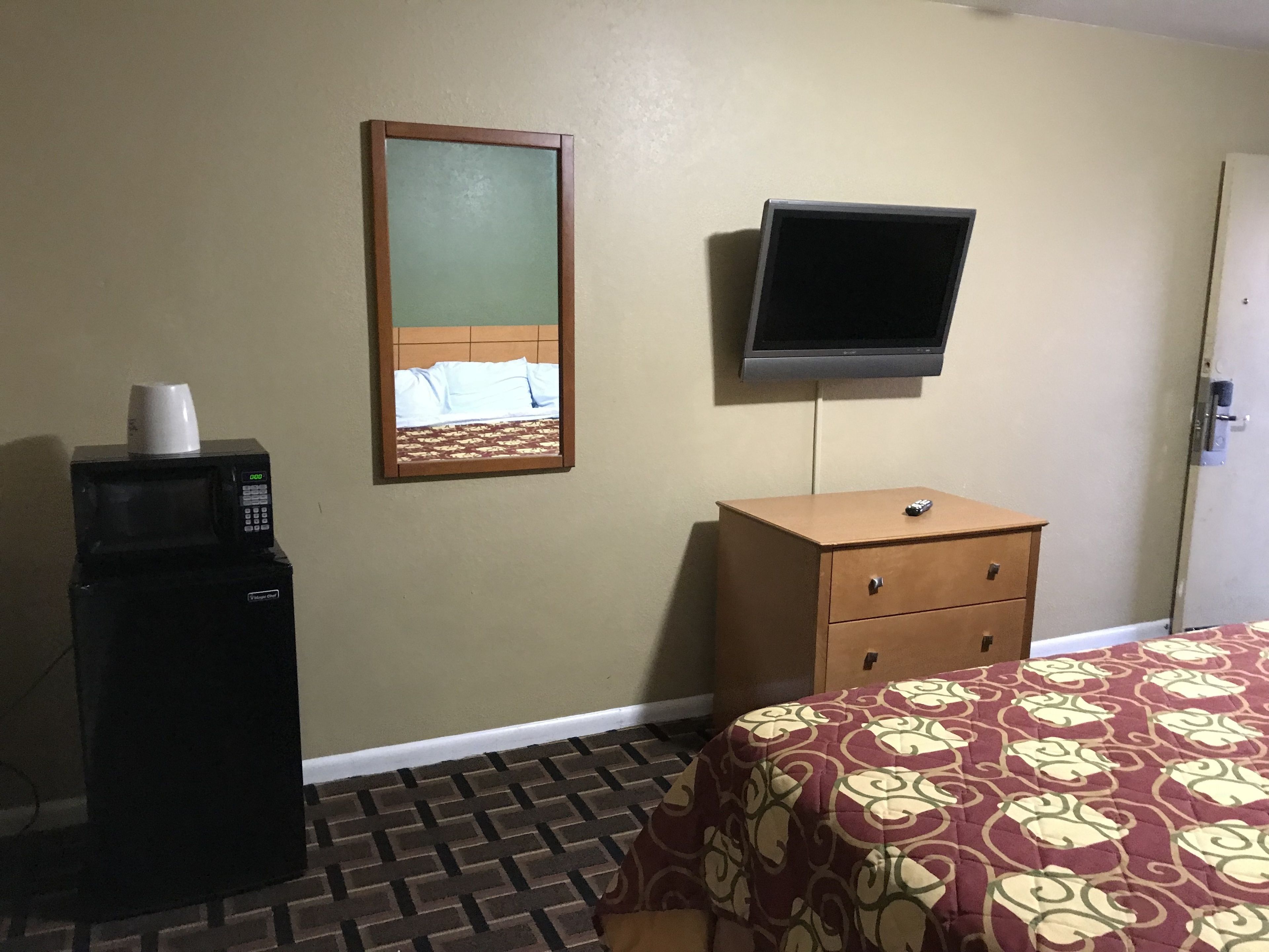 A hotel room with a bed, a dresser, a television mounted on the wall, and a microwave on the floor.