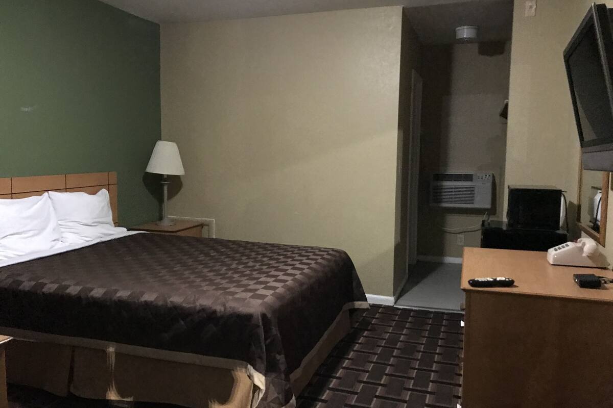 A hotel room with a bed, a desk with a telephone, a lamp, and a television.