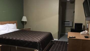 Een hotelkamer met een bed, een bureau met telefoon, een lamp en een televisie.