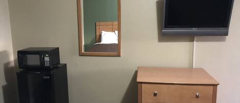 Habitación de hotel con microondas, pequeño refrigerador, cómoda de madera, espejo y televisor montado en la pared.