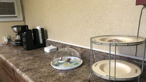Una encimera de cocina con una cafetera, un hervidor y un microondas. Hay una pila de servilletas blancas y un bol de vidrio sobre la encimera.