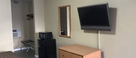 Una habitación de hotel con cama, cómoda, televisor montado en la pared y microondas sobre un mueble.