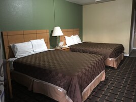 Habitación de hotel con dos camas, cada una con cubrecama marrón, almohadas blancas y una mesita de noche con lámpara y teléfono.