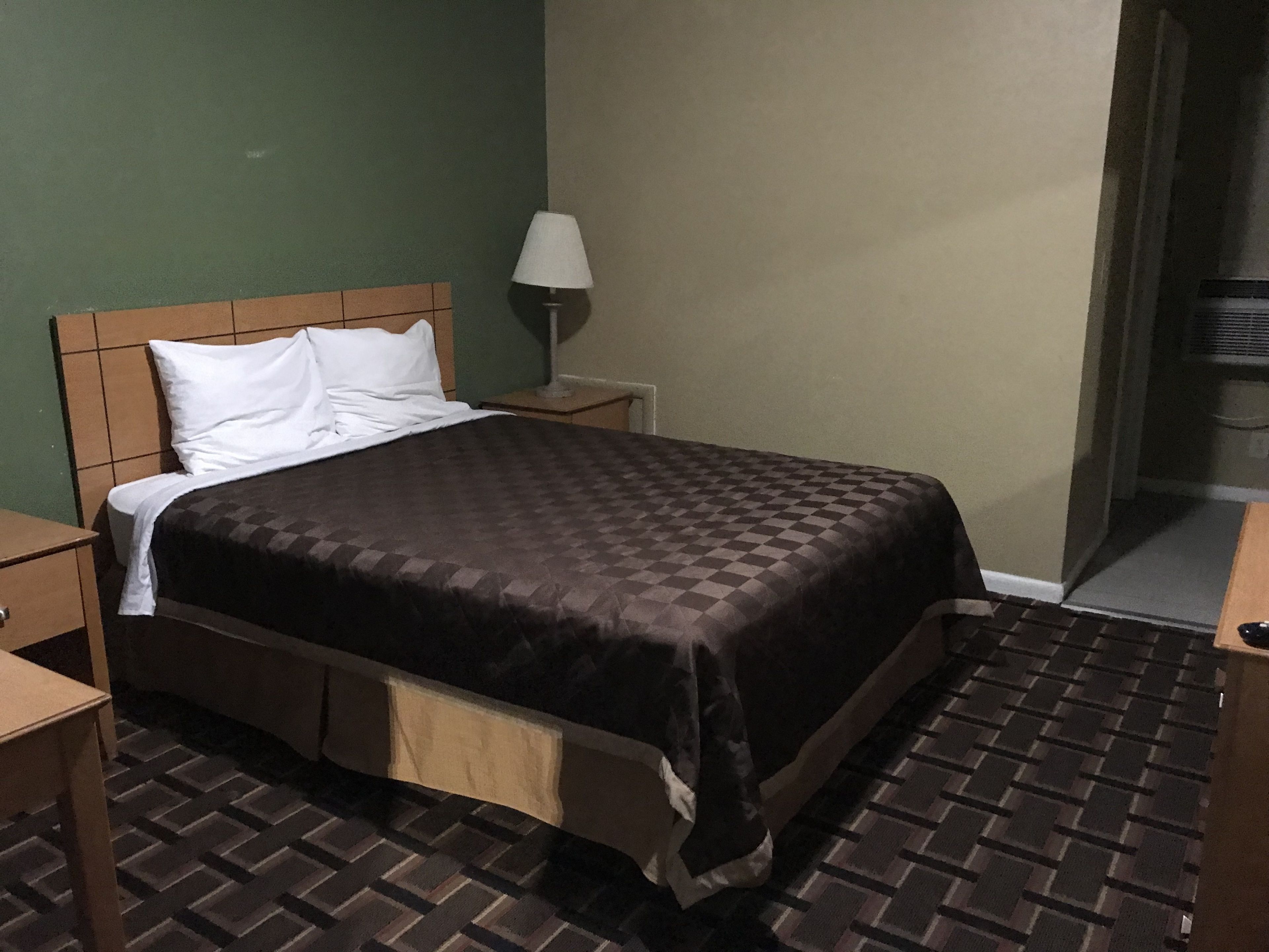 A neatly made bed with a checkered bedspread, a bedside lamp, and a nightstand.