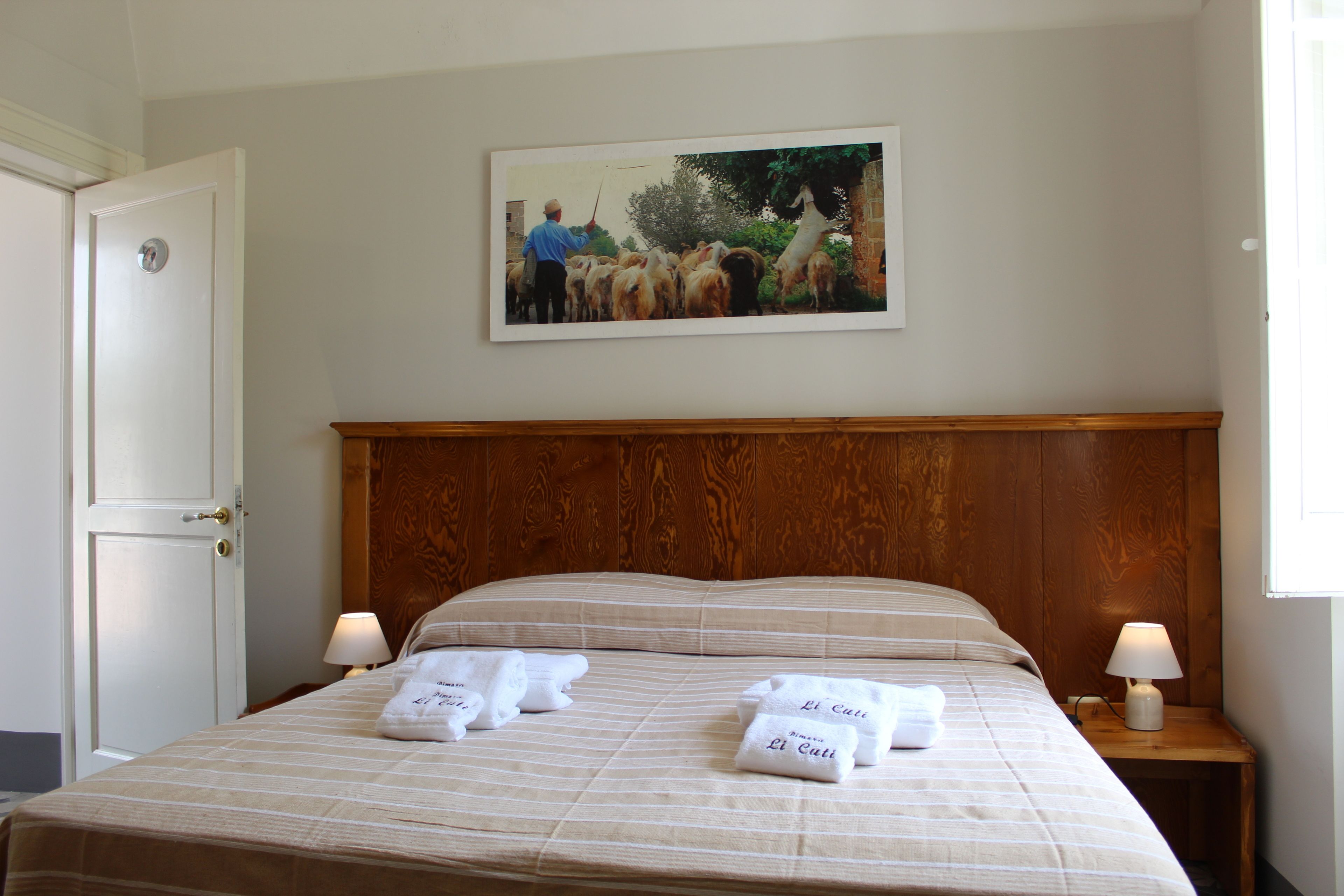 Una habitación de hotel con cabecera de madera, cama con cubrecama a rayas, dos lámparas de noche y un cuadro enmarcado en la pared.